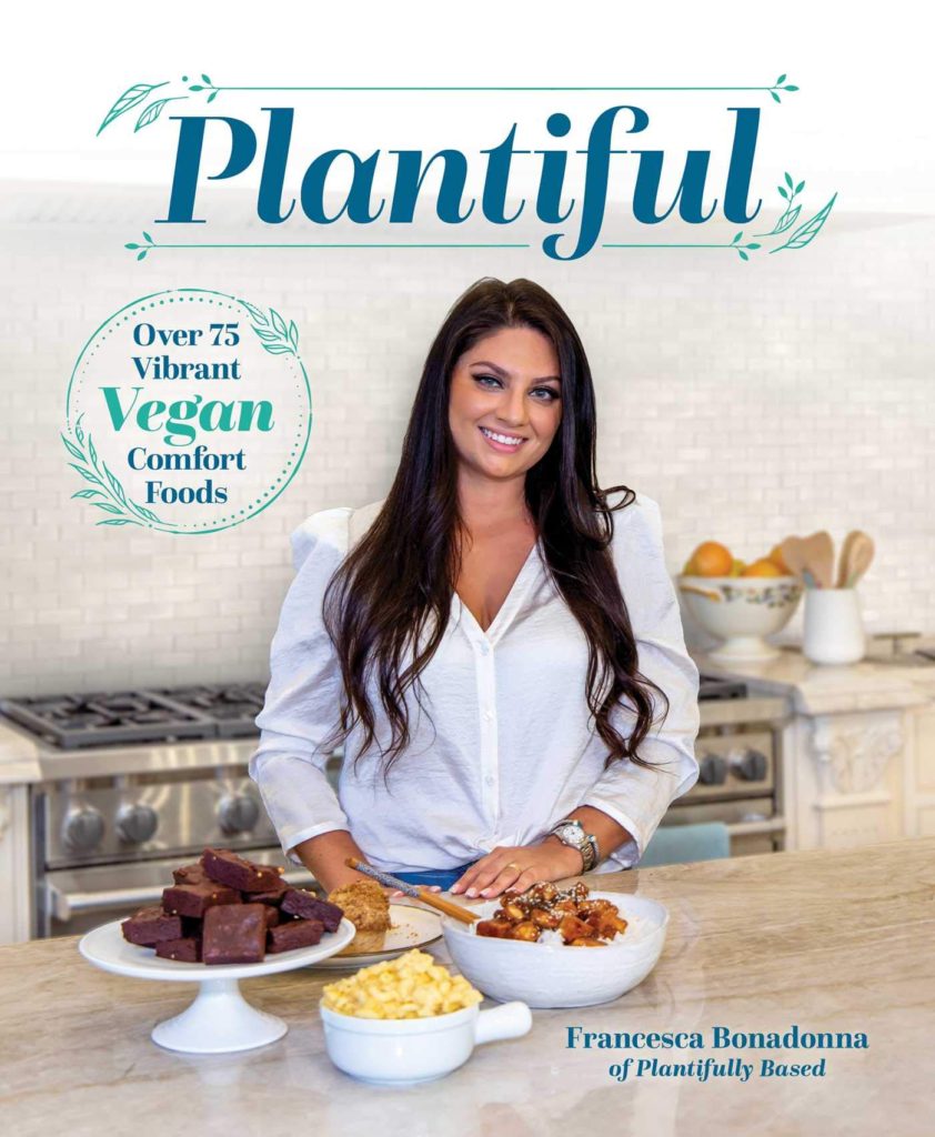 cover of my cookbook Plantiful, girl standing in kitchen with food around her, white shirt, and jeans on