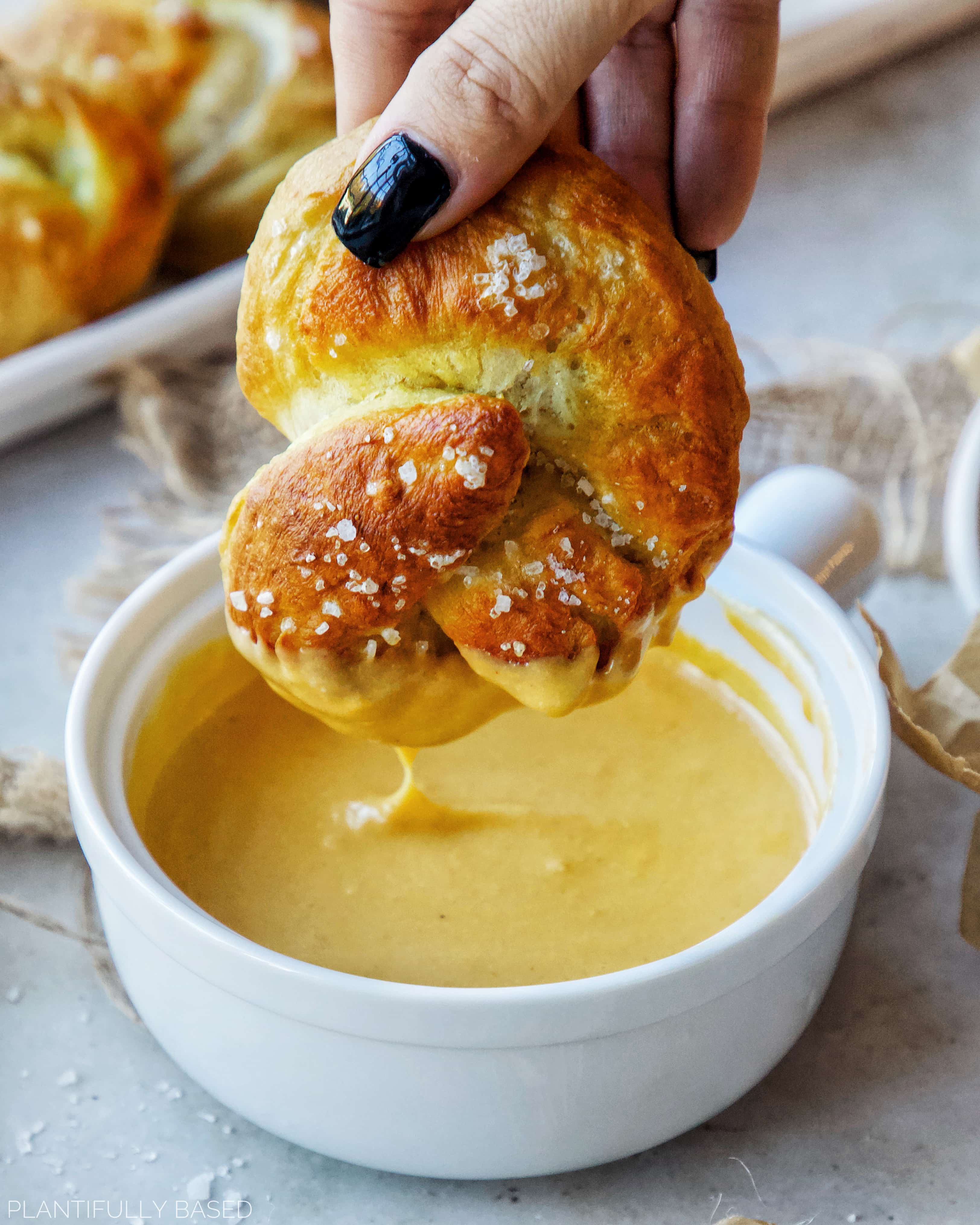image of homemade soft pretzels being dipped in vegan cheese sauce