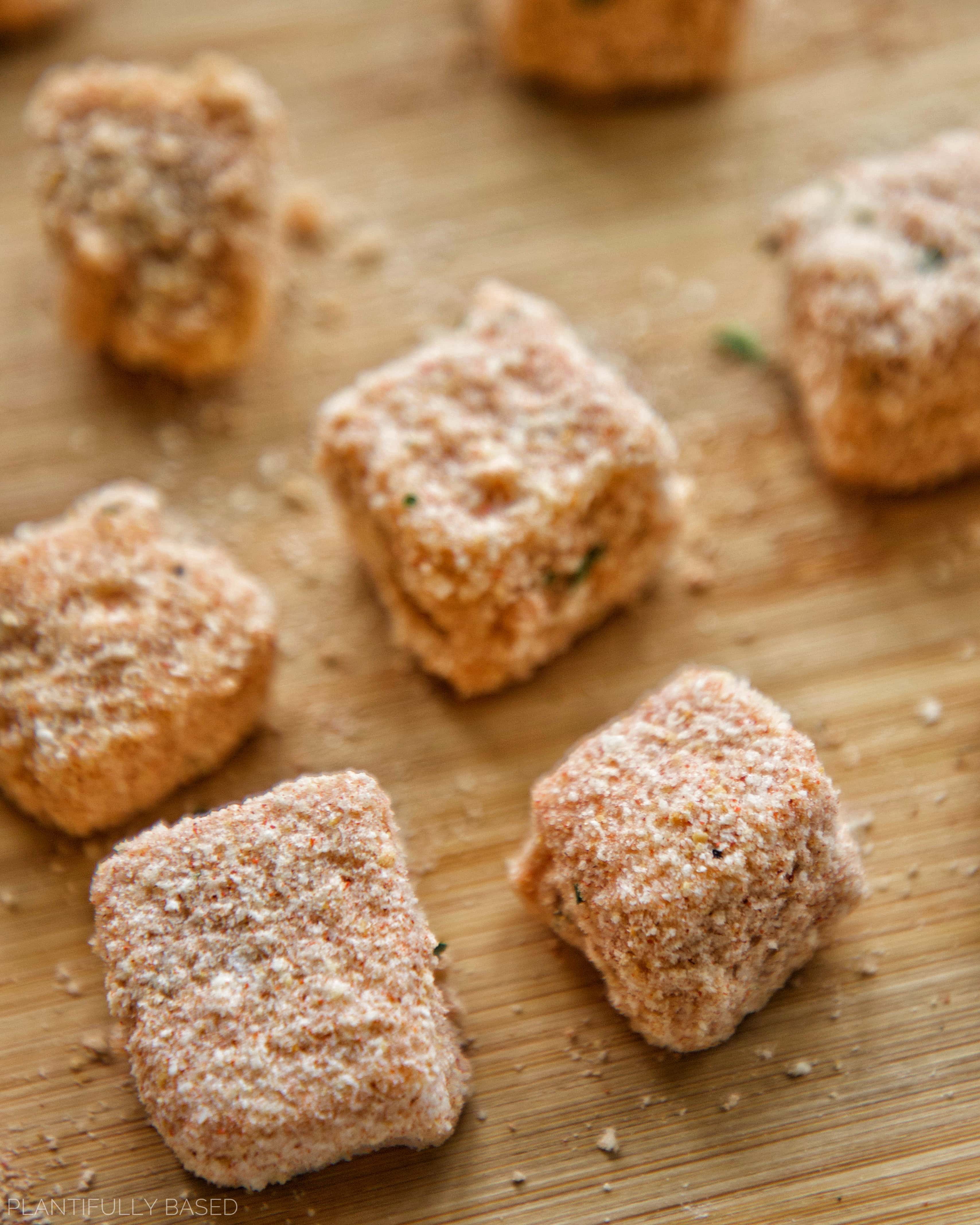 vegan mozzarella bites before air frying, covered in breadcrumbs on a cutting board