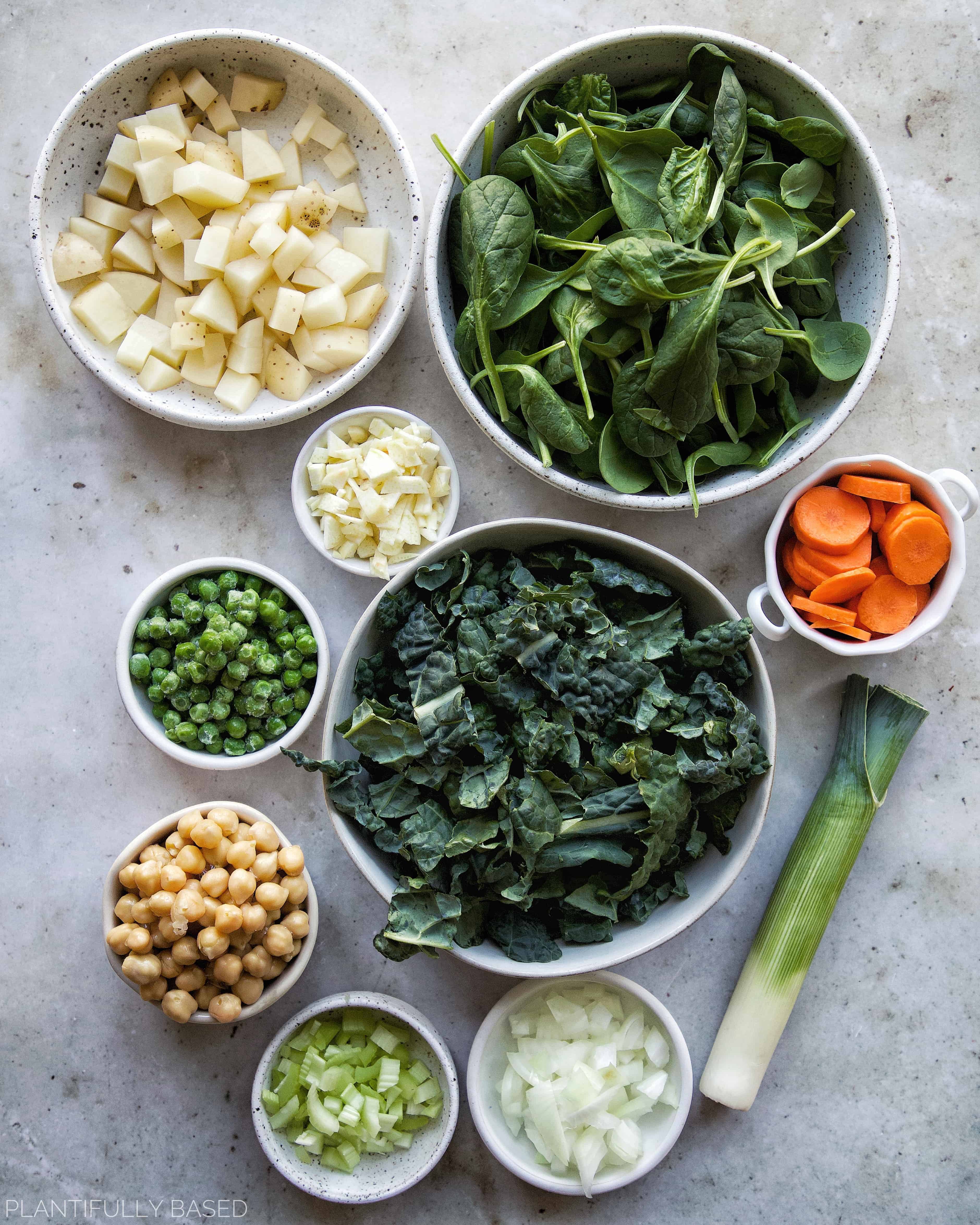 ingredients for spring green minestrone soup - potatoes, spinach, garlic, peas, carrots, kale, chickpeas, and leeks