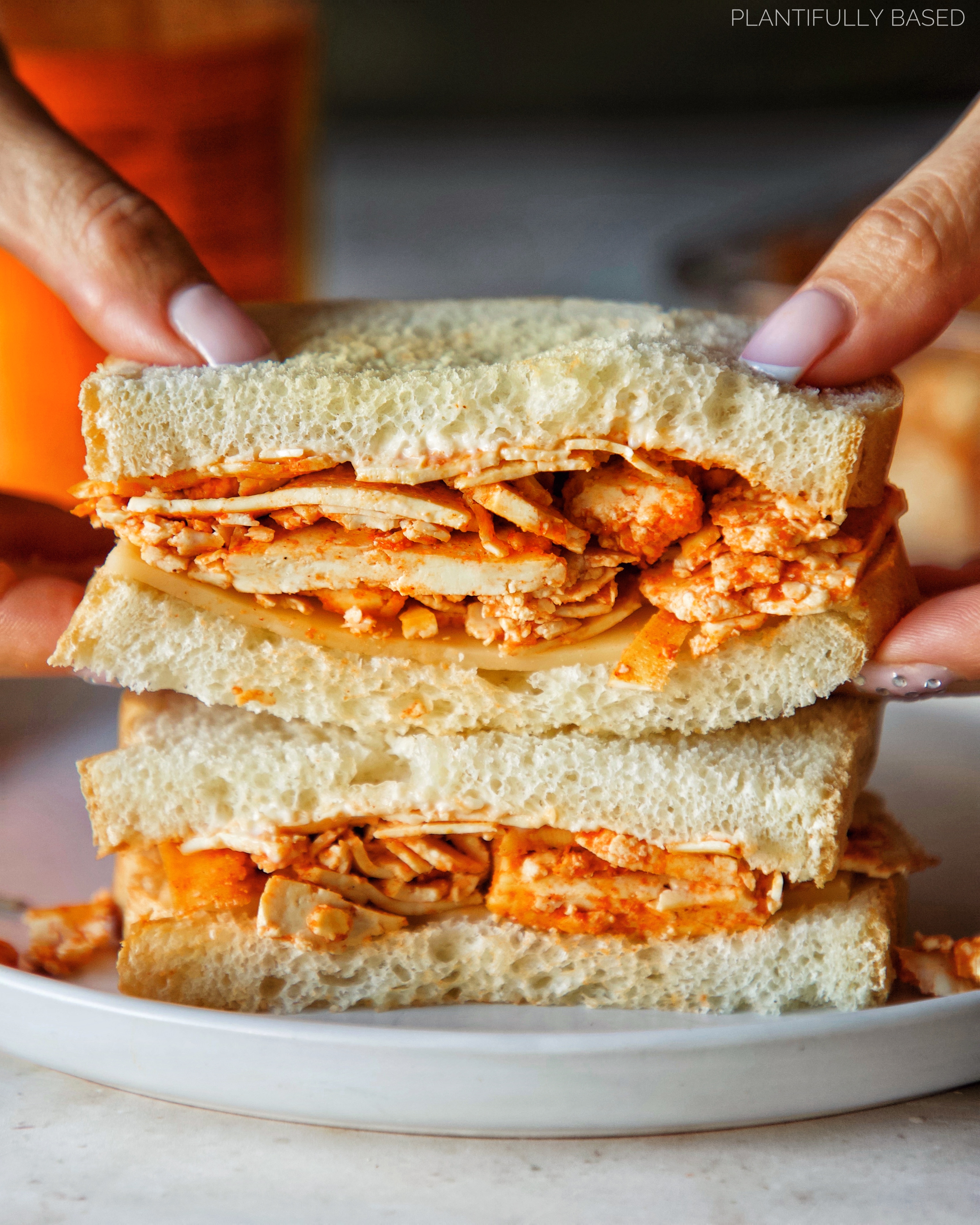 image of tofu lunch meat in a sandwich with hands holding it