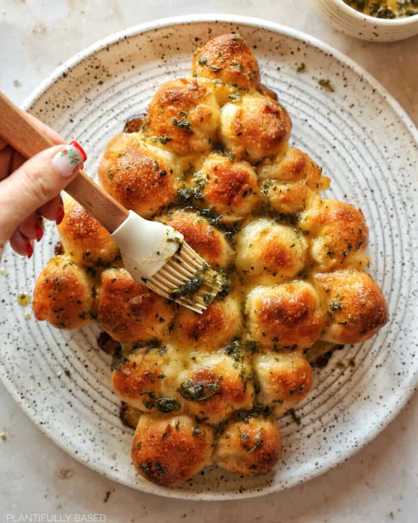 christmas tree pull apart bread being brushed with melted vegan butter
