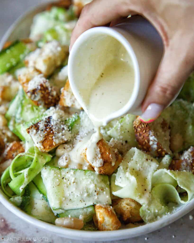dressing being poured over Shaved Zucchini Caesar Salad (Vegan)