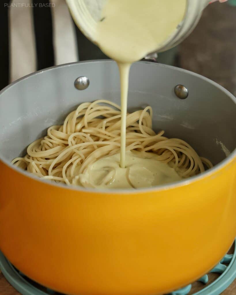 pouring the vegan alfredo sauce over the pasta