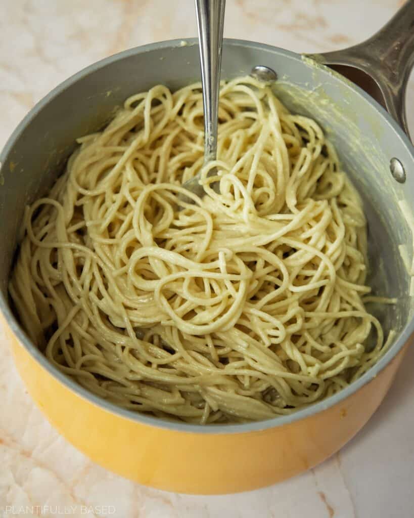 mixing the vegan alfredo sauce with pasta